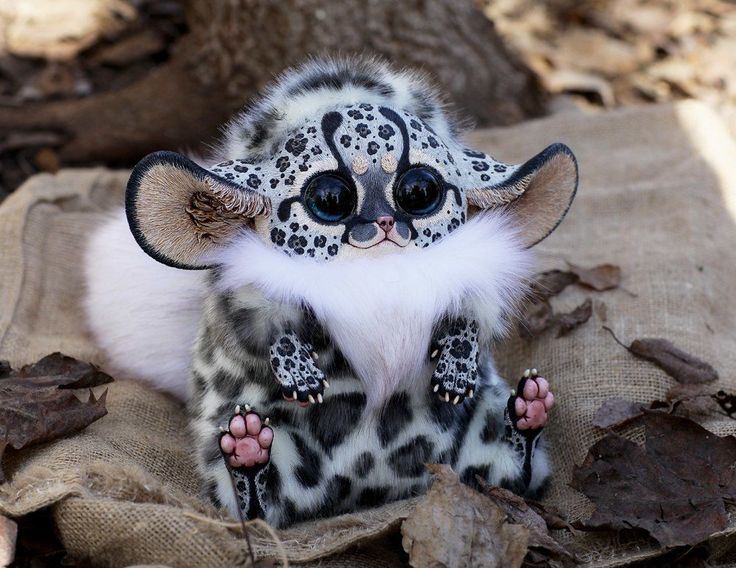 a stuffed animal that looks like a leopard with big eyes sitting on top of a blanket