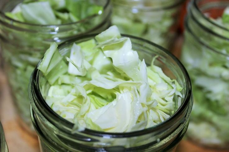 several mason jars filled with lettuce on top of a wooden table