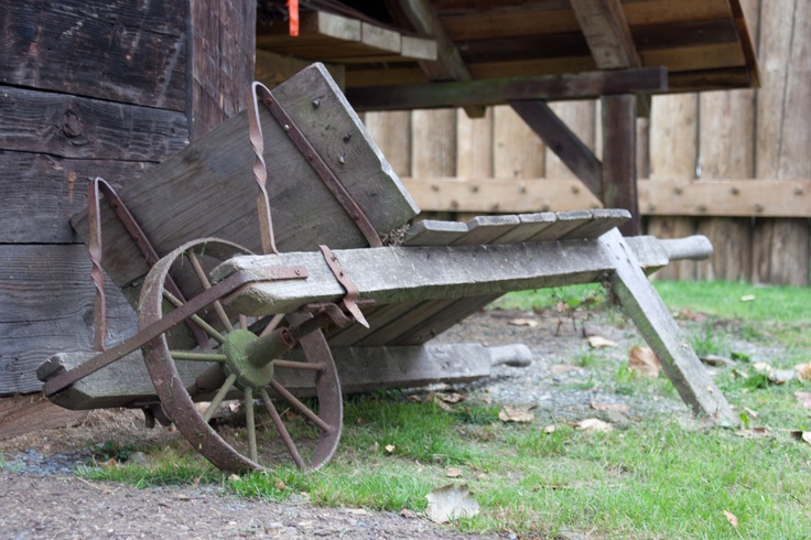 an old wooden wagon sitting in the grass next to a building with wood sidings