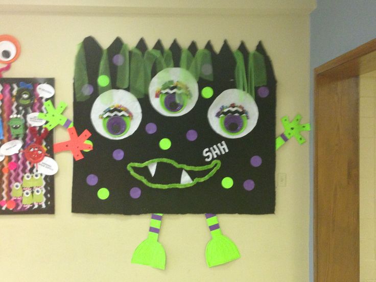 a bulletin board with paper monsters on it and other items hanging from the wall behind it