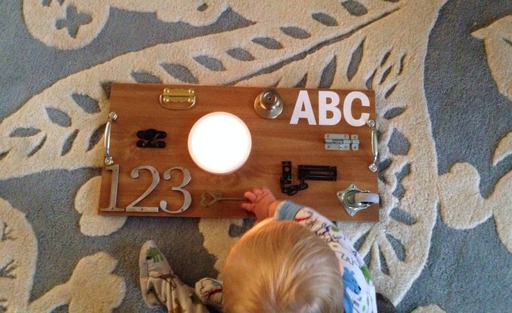 a toddler playing with a light on a wooden plaque that says abc 123 in it