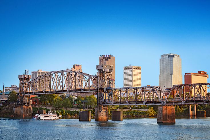 a large bridge spanning over a river with tall buildings in the background and a boat passing under it