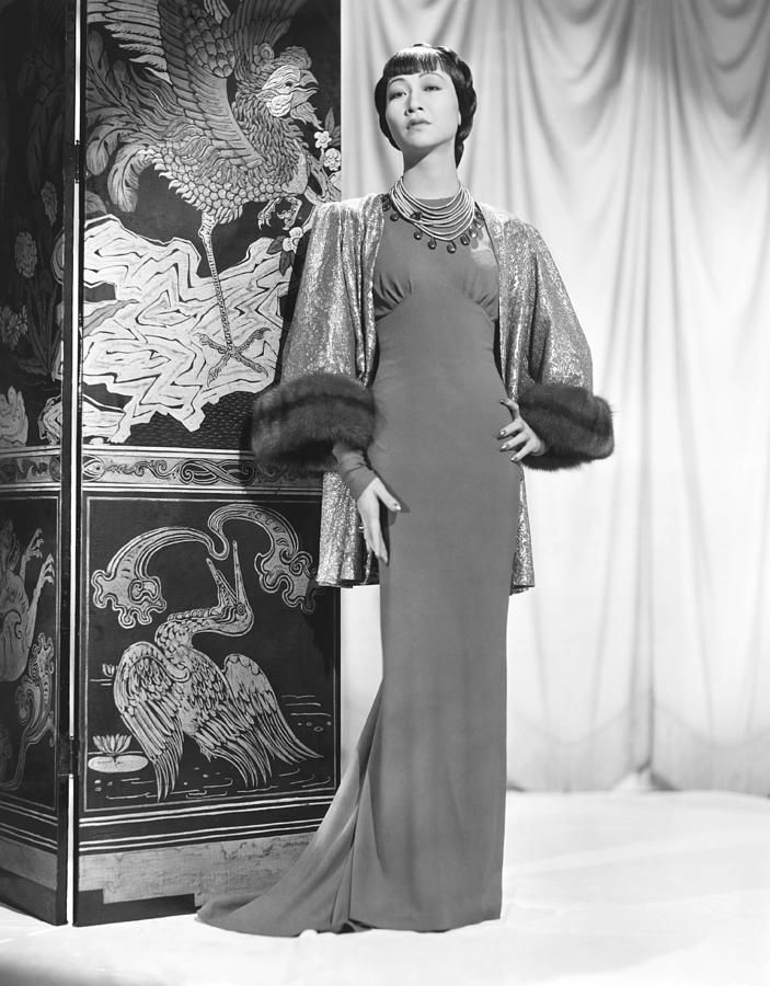 a woman in a long dress standing next to a wall with an elaborate painting on it