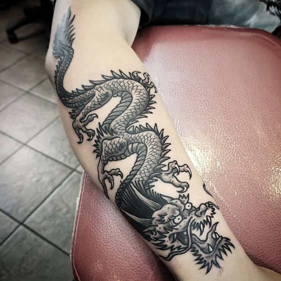 a dragon tattoo on the arm of a woman sitting in a chair with her legs crossed