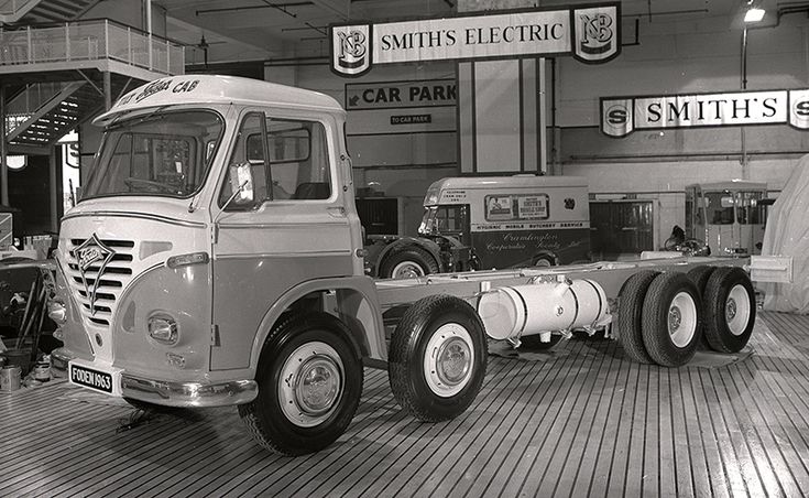 an old semi truck is parked in a garage with other trucks and equipment behind it