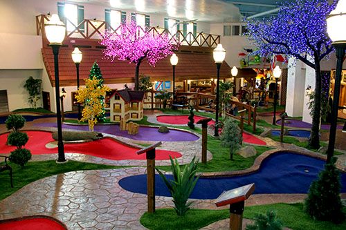 an indoor miniature golf course with artificial grass and fake trees in the center, surrounded by lights