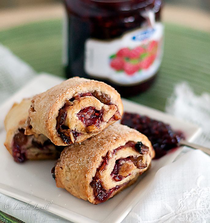 two pastries sitting on top of a white plate next to berries and jam in a jar