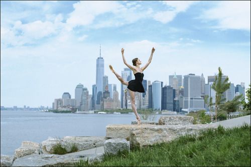 a woman in a black leotard is standing on some rocks near the water