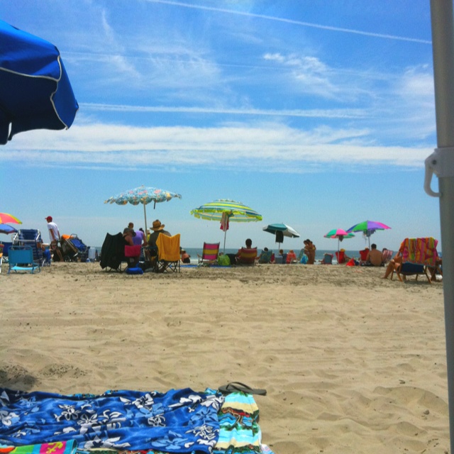 people sitting on the beach under umbrellas and chairs with blue skies in the background