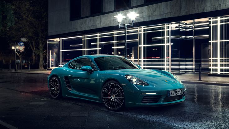 a blue sports car parked in front of a building at night with its lights on