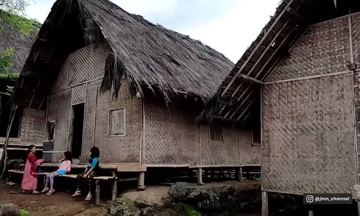 three people sitting outside of wooden houses with thatched roofs