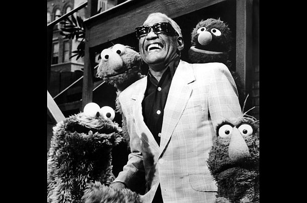 an older man in a suit and sunglasses standing next to sesame characters