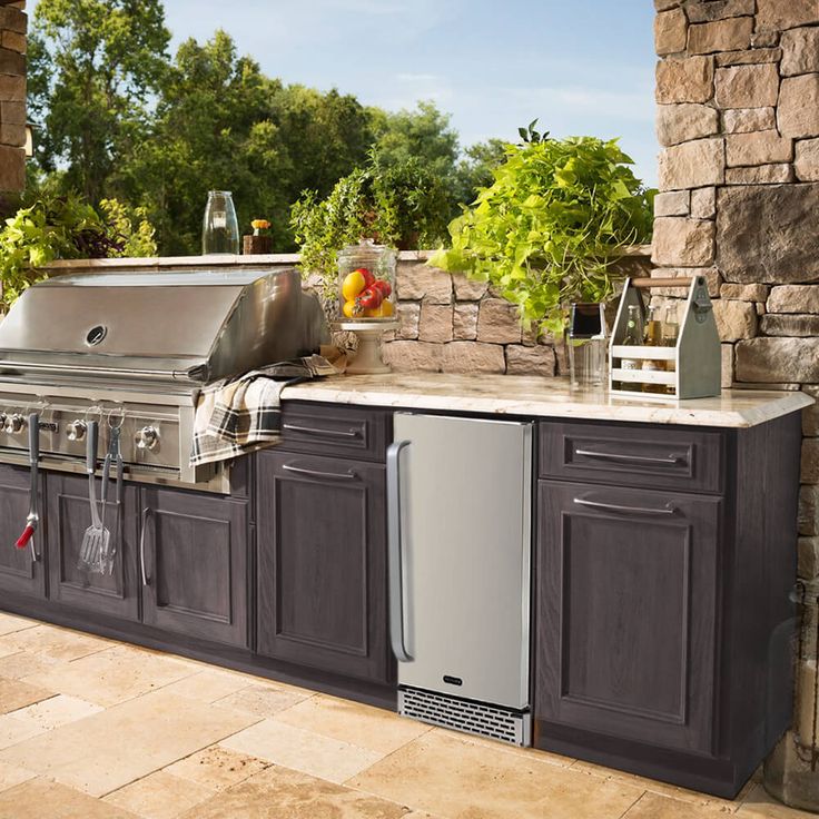 an outdoor kitchen with stainless steel appliances and granite counter tops, surrounded by stone walls