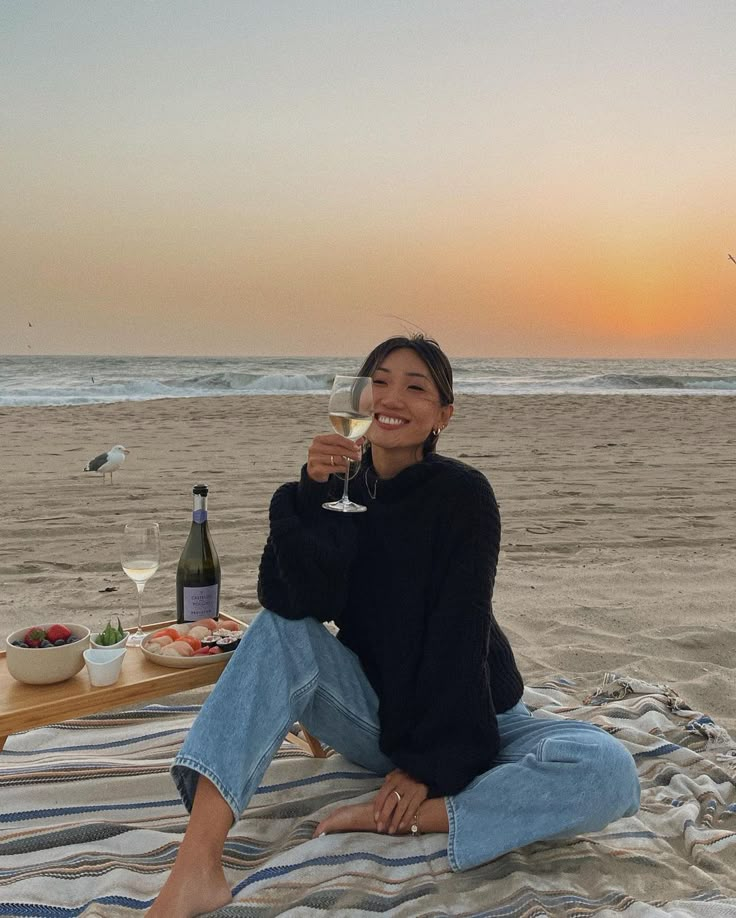 a woman sitting on top of a beach holding a glass of wine