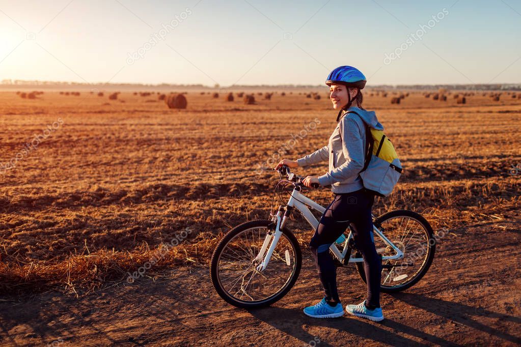 Young bicyclist riding in autumn field with haystacks at sunset. Woman ...