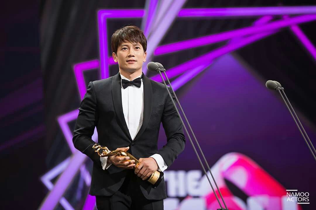 a man in a tuxedo holding an award at the awards stage with microphones