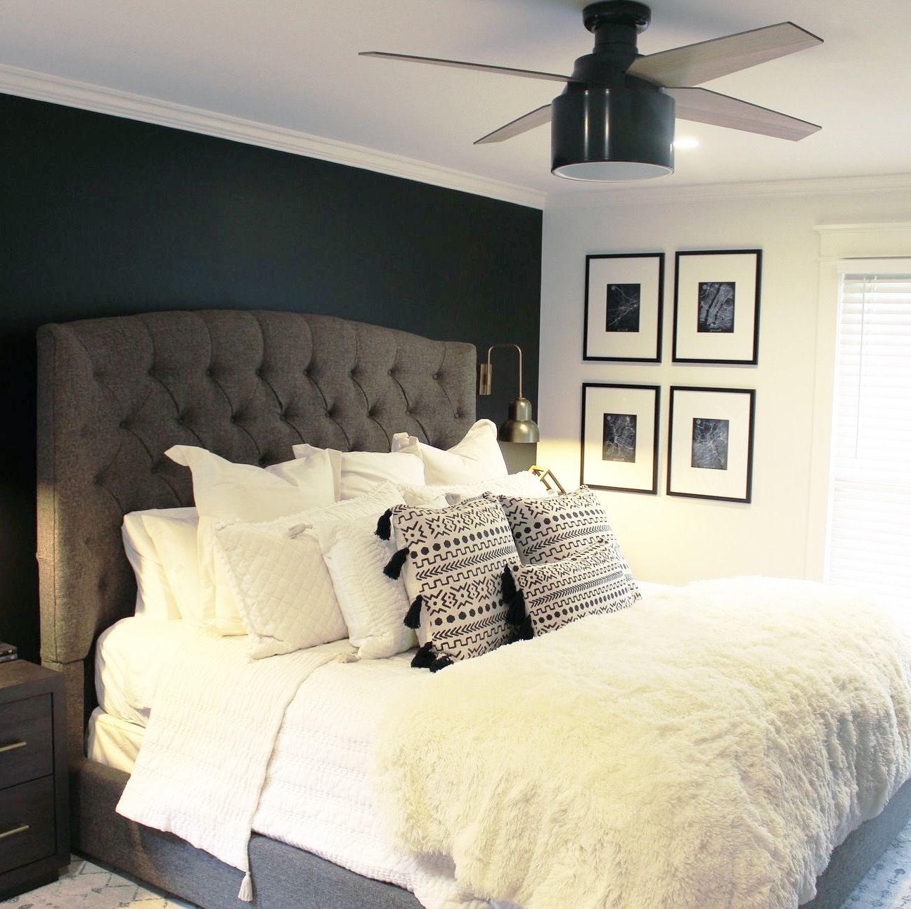 Black accent wall with upholstered bed. Modern fan and frames art