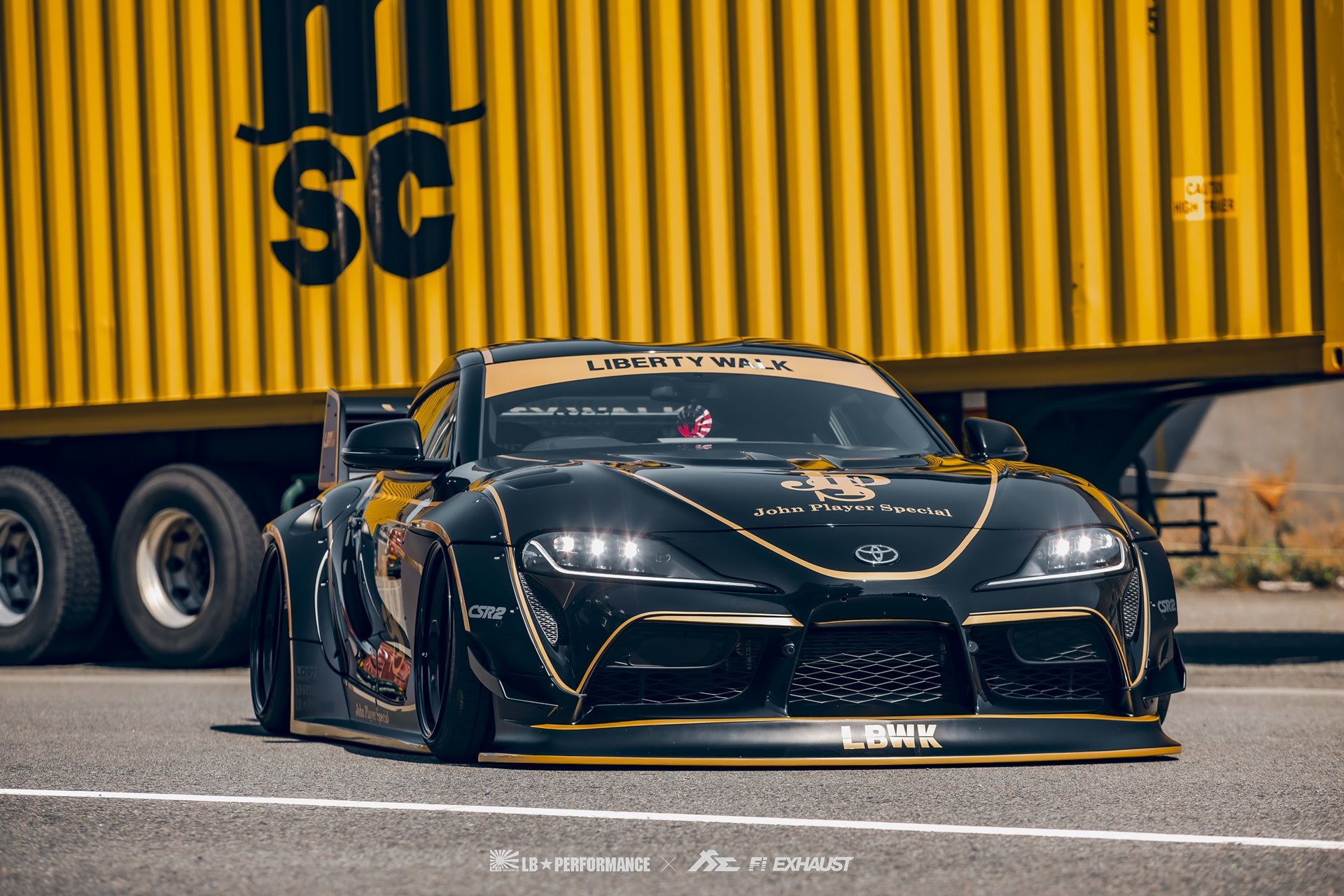 a black and yellow sports car driving down the road next to a large ...