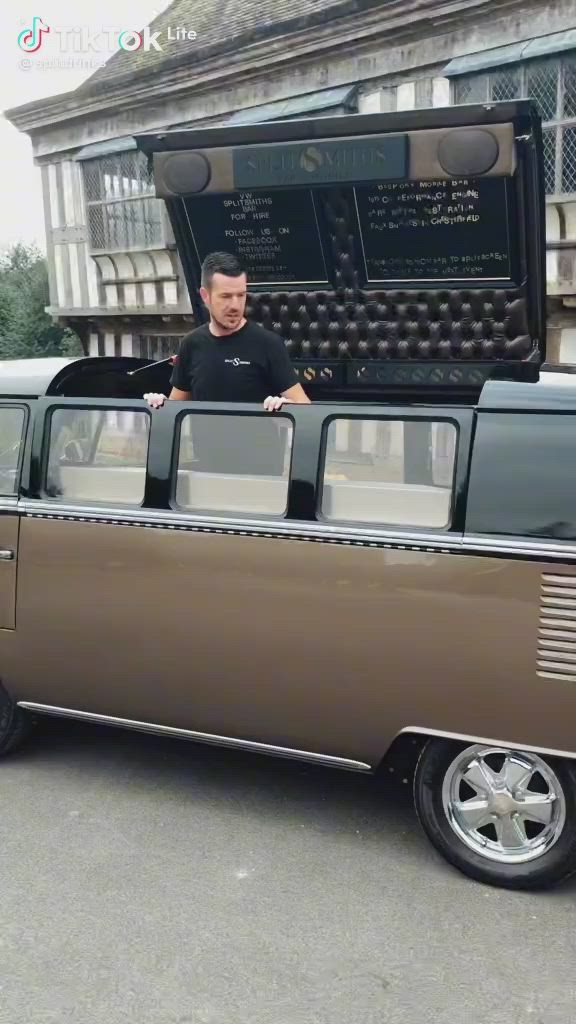 This may contain: a man standing in front of a brown and black vw bus with an open trunk