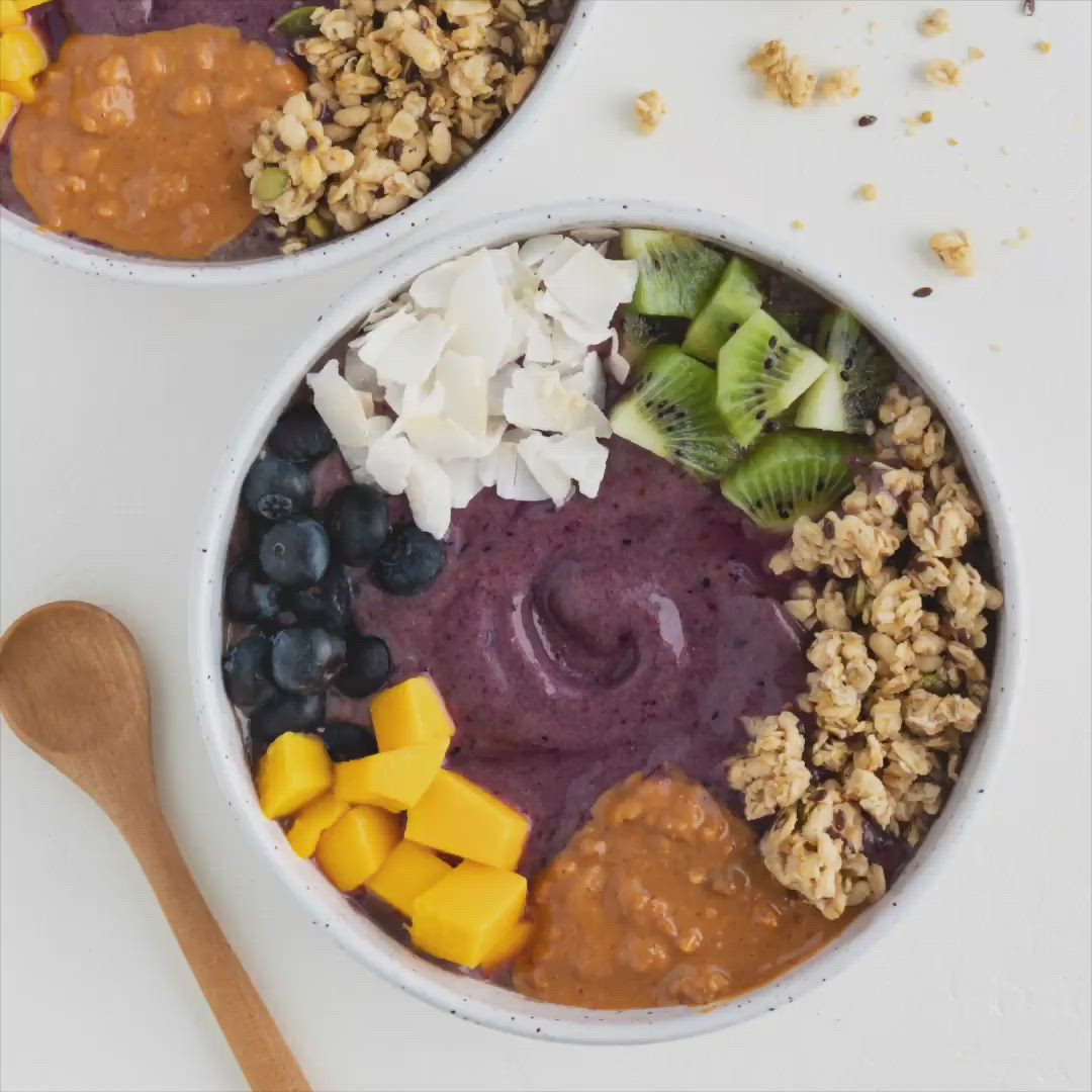 This may contain: two bowls filled with fruit, nuts and granola on top of a white table