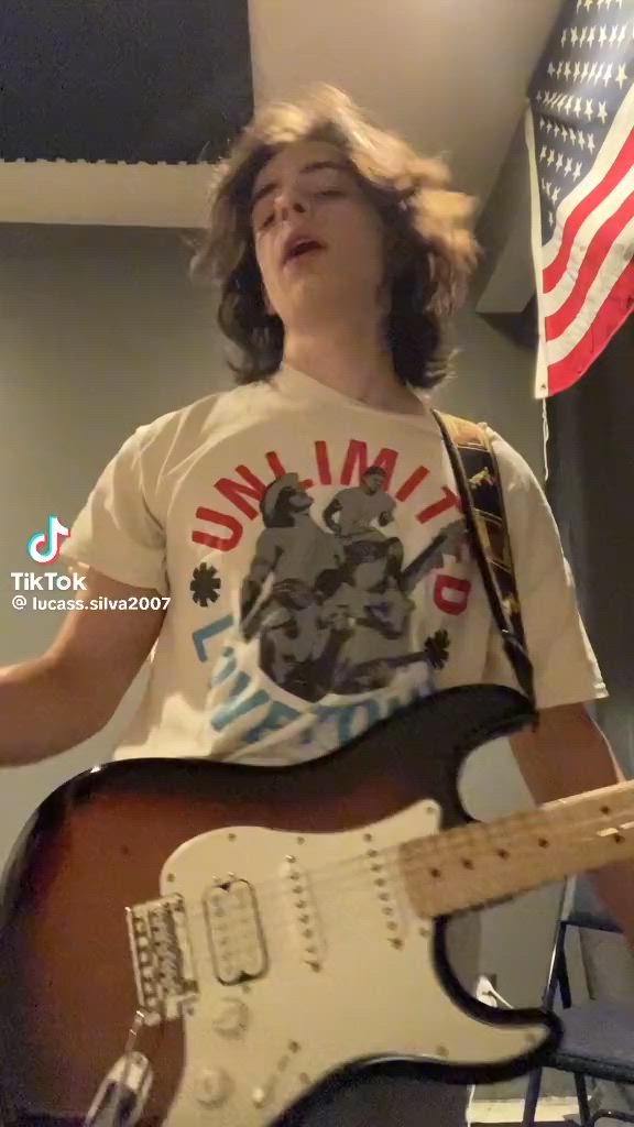 This may contain: a young man playing an electric guitar in front of the american flag and holding it up