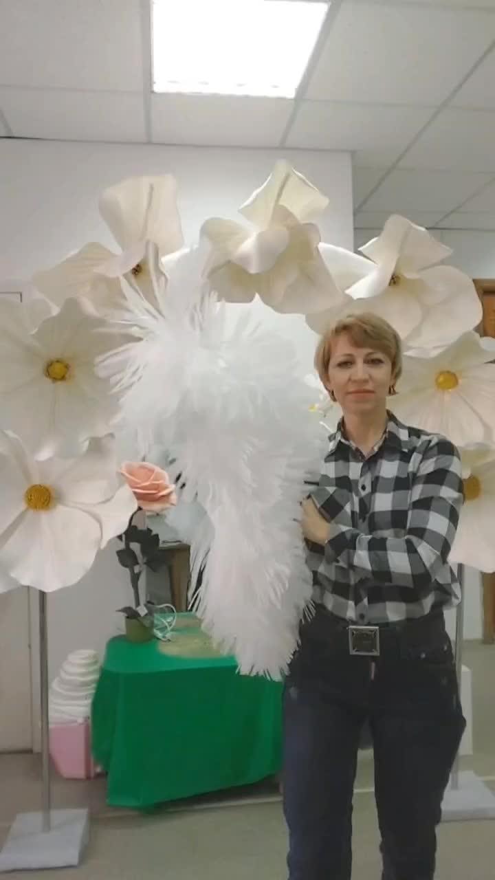 This may contain: a woman standing next to large white flowers in an office building with her hands on her hips