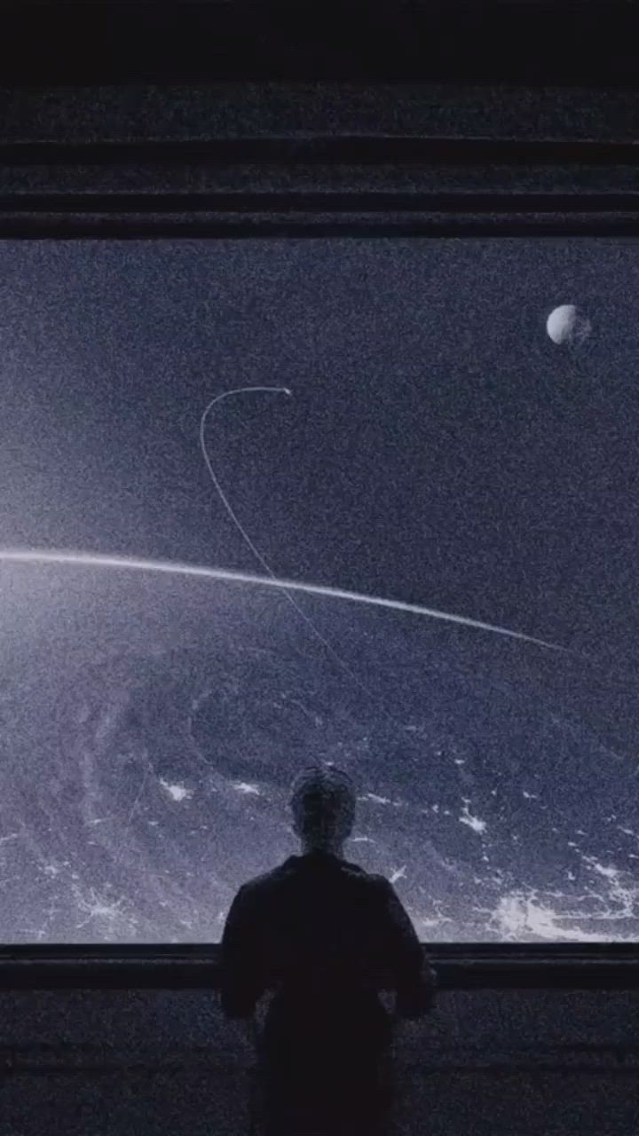 This may contain: a man standing in front of a window looking at an image of saturn and the moon