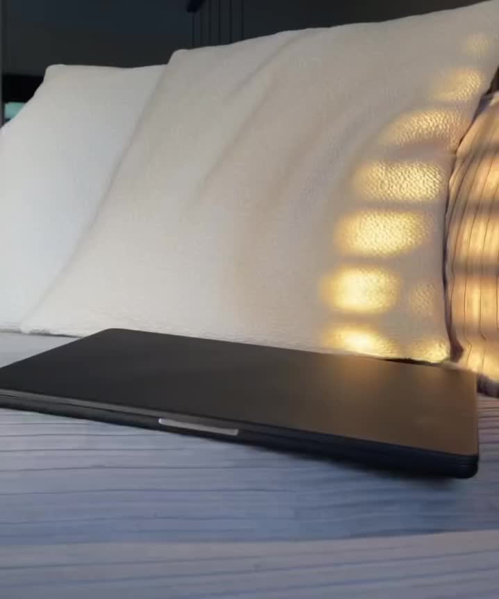 This may contain: a laptop computer sitting on top of a bed next to white pillows and pillow cases