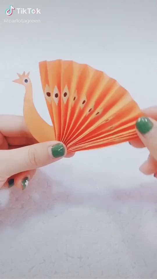 This may contain: a hand holding a blue and orange paper fan next to a small bird on it