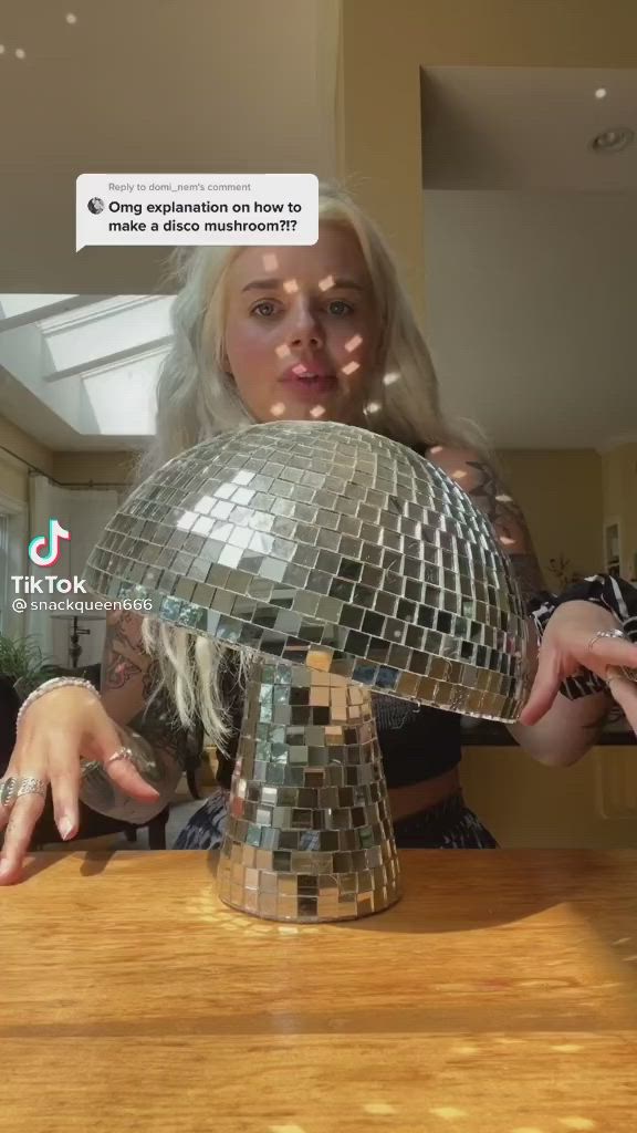 This may contain: a woman holding a disco ball on top of a wooden table