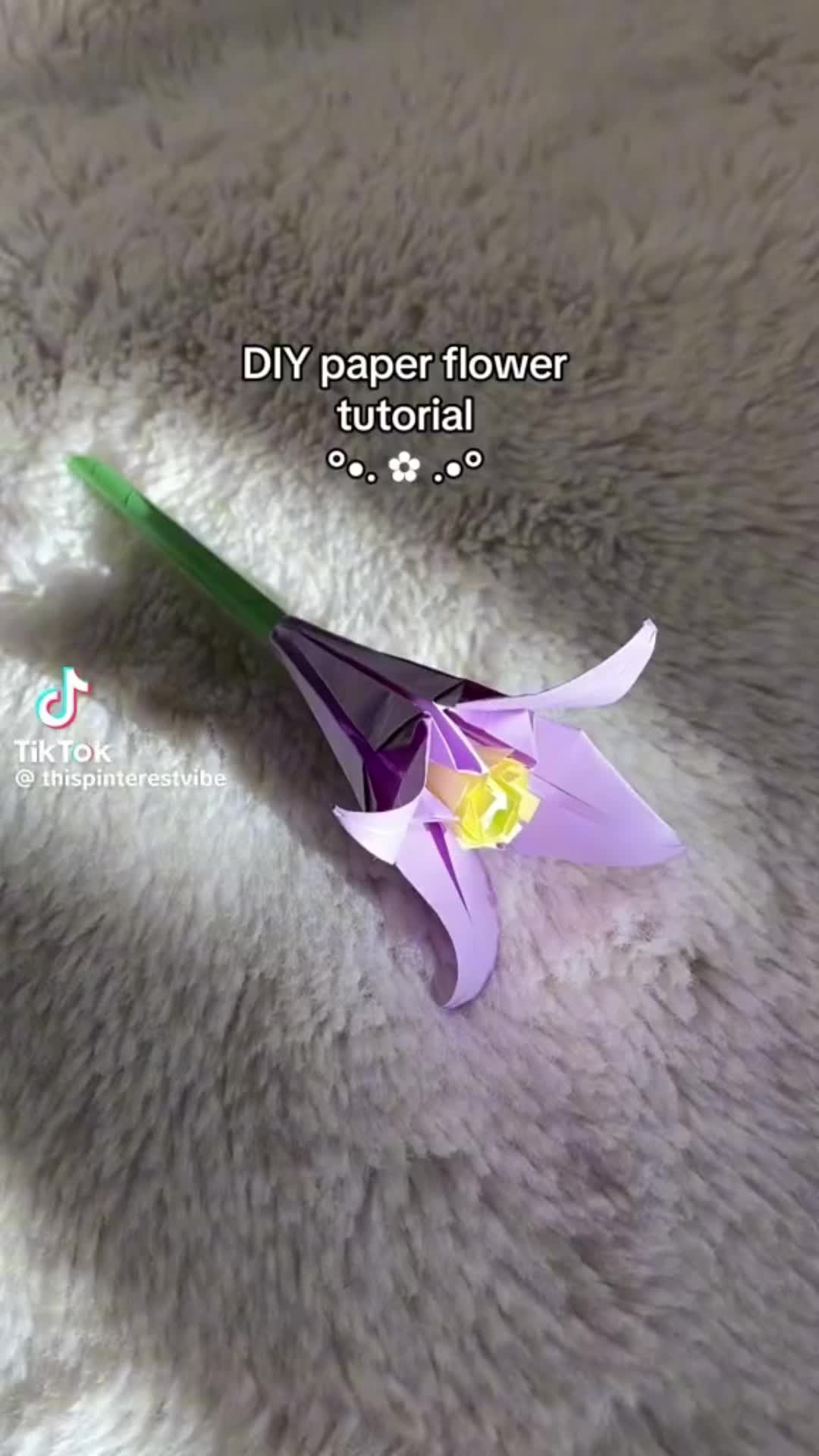 This may contain: an origami flower sitting on top of a fluffy white blanket with the words diy paper flower tutorial written below it