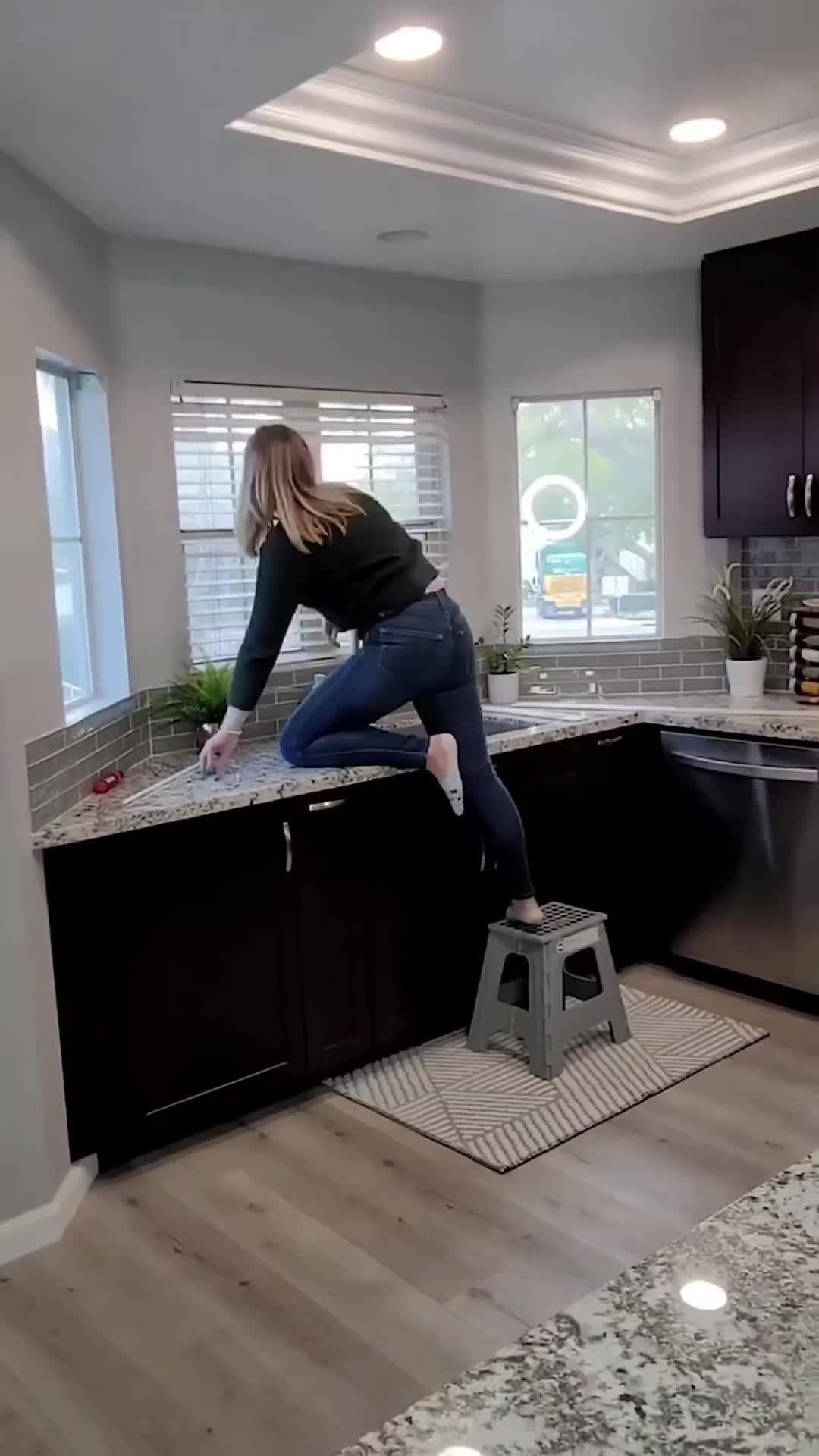 This may contain: a woman standing on top of a stool in a kitchen