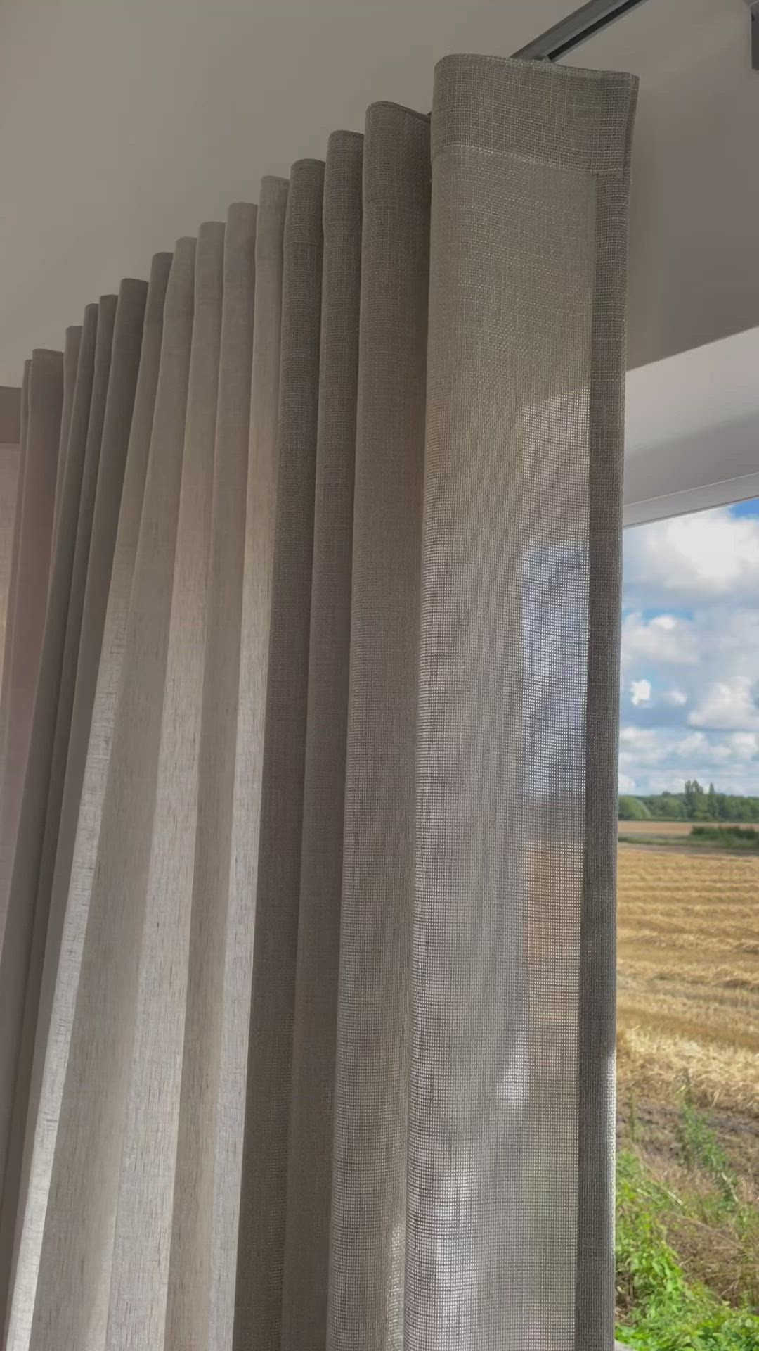 This may contain: an open window with curtains in front of a wheat field and blue sky behind it