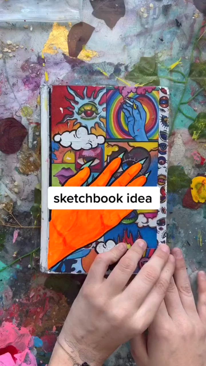 This may contain: a person is holding up a sketchbook in front of some paint and paper collages