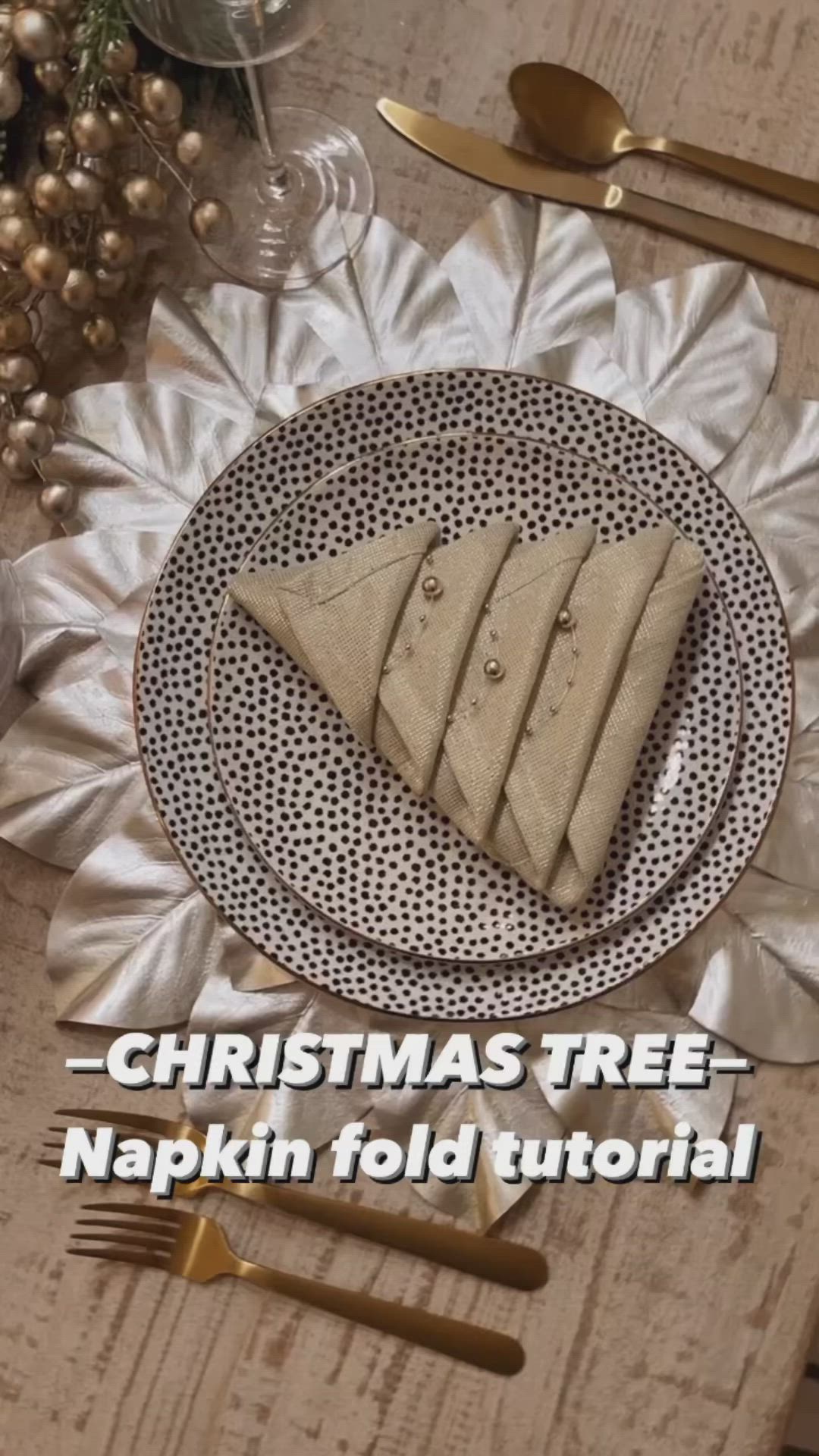 This may contain: a christmas tree napkin on top of a plate next to a candle and some silverware