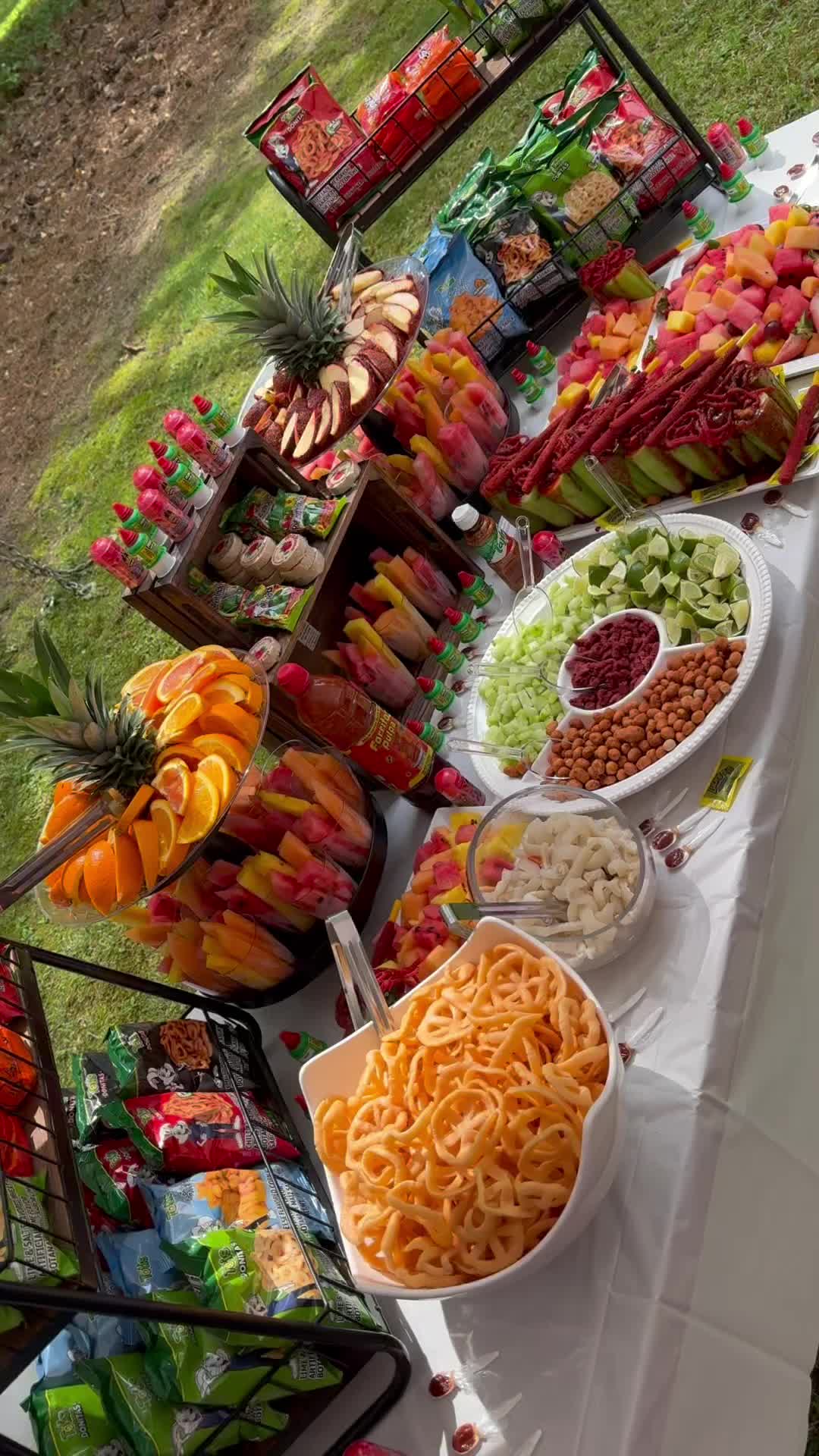 This may contain: an assortment of food is displayed on a buffet table with white cloths and fruit