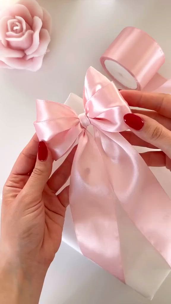 This may contain: a woman is holding a pink ribbon in front of a rose on a white table