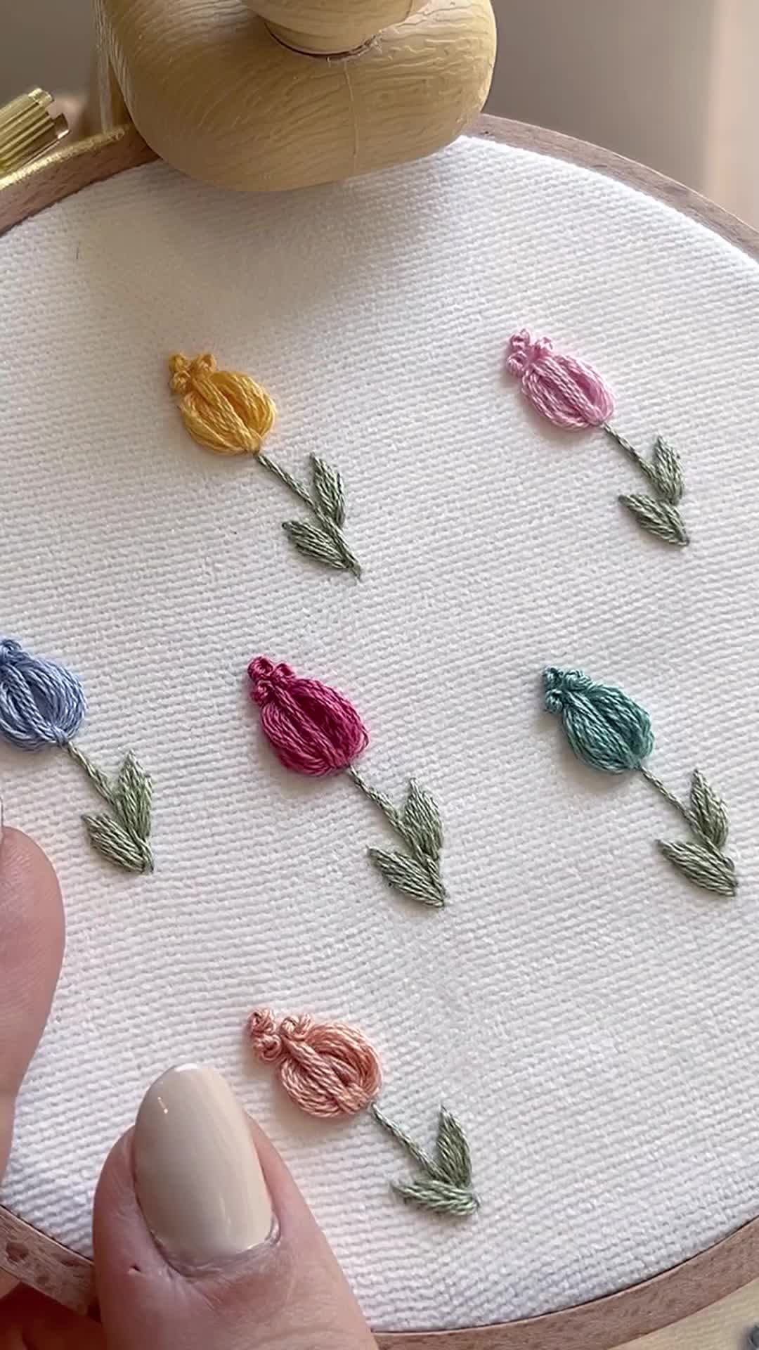 This may contain: a person is stitching flowers on a white piece of fabric with a wooden frame