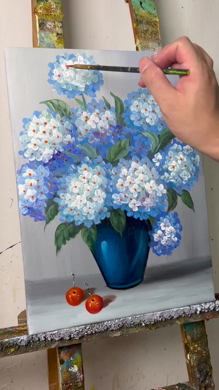 This may contain: a painting of blue and white flowers in a blue vase on an easel with paintbrushes