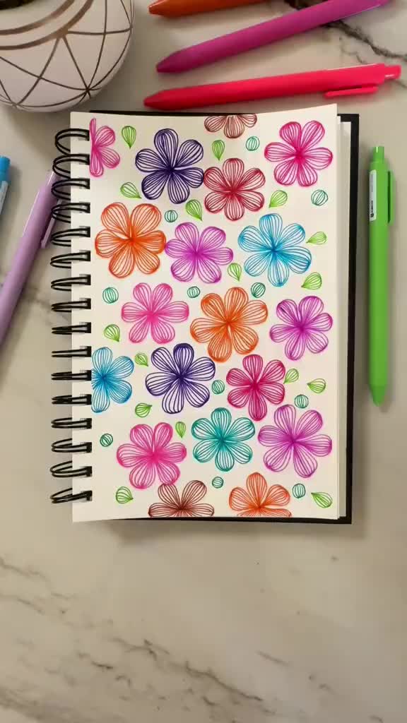 This may contain: a notebook with colorful flowers on it next to markers, pens and a potted plant