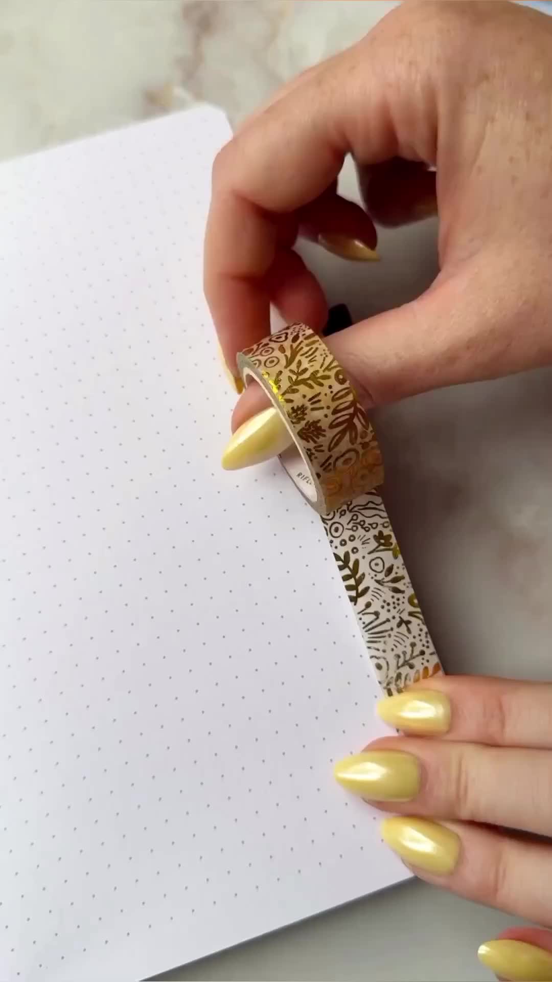 This may contain: a woman with yellow nails holding onto a piece of paper that has gold foil on it