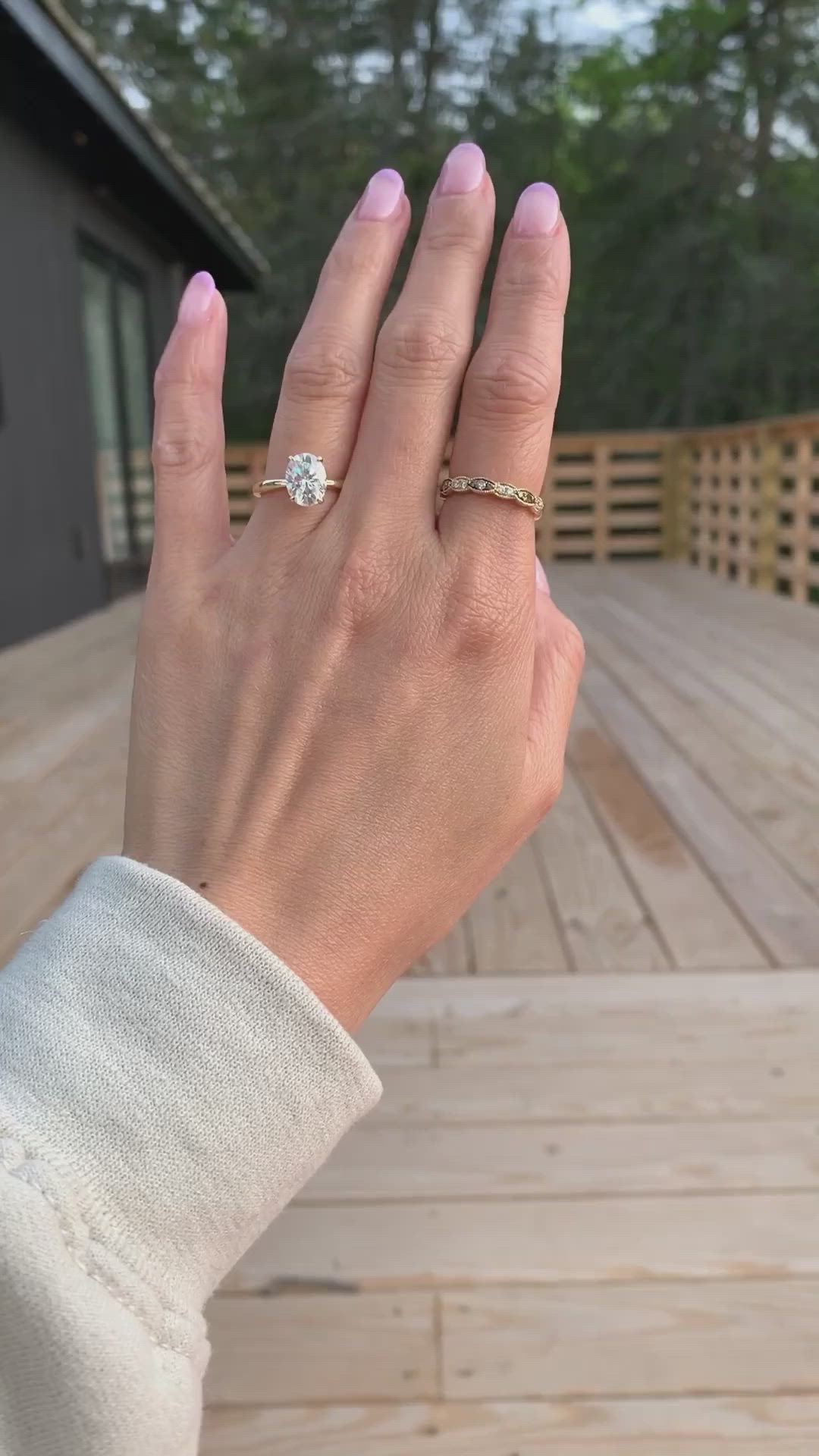 This may contain: a woman's hand with a diamond ring on her finger, standing in front of a wooden deck