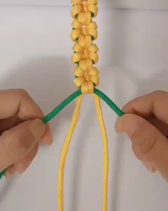 This may contain: two hands are working on a piece of yellow fabric with green string and flowers attached to it