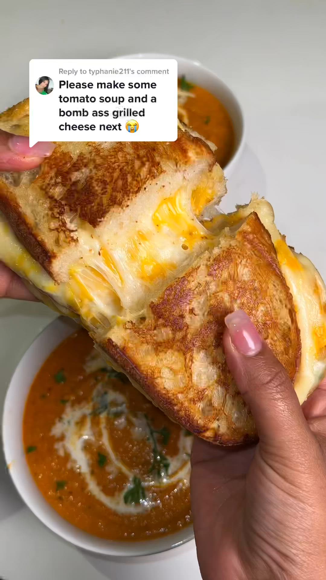 This may contain: someone is holding up a grilled cheese sandwich with soup in the bowl behind it