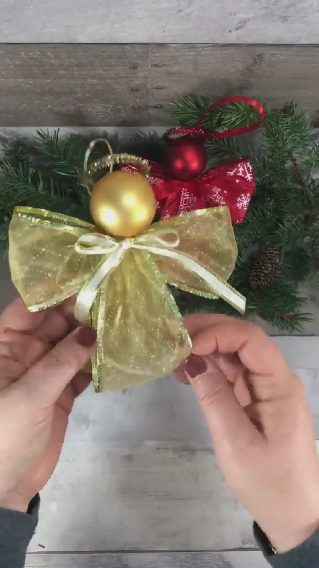 This may contain: two hands holding a christmas ornament in front of a pine tree with red and gold ornaments