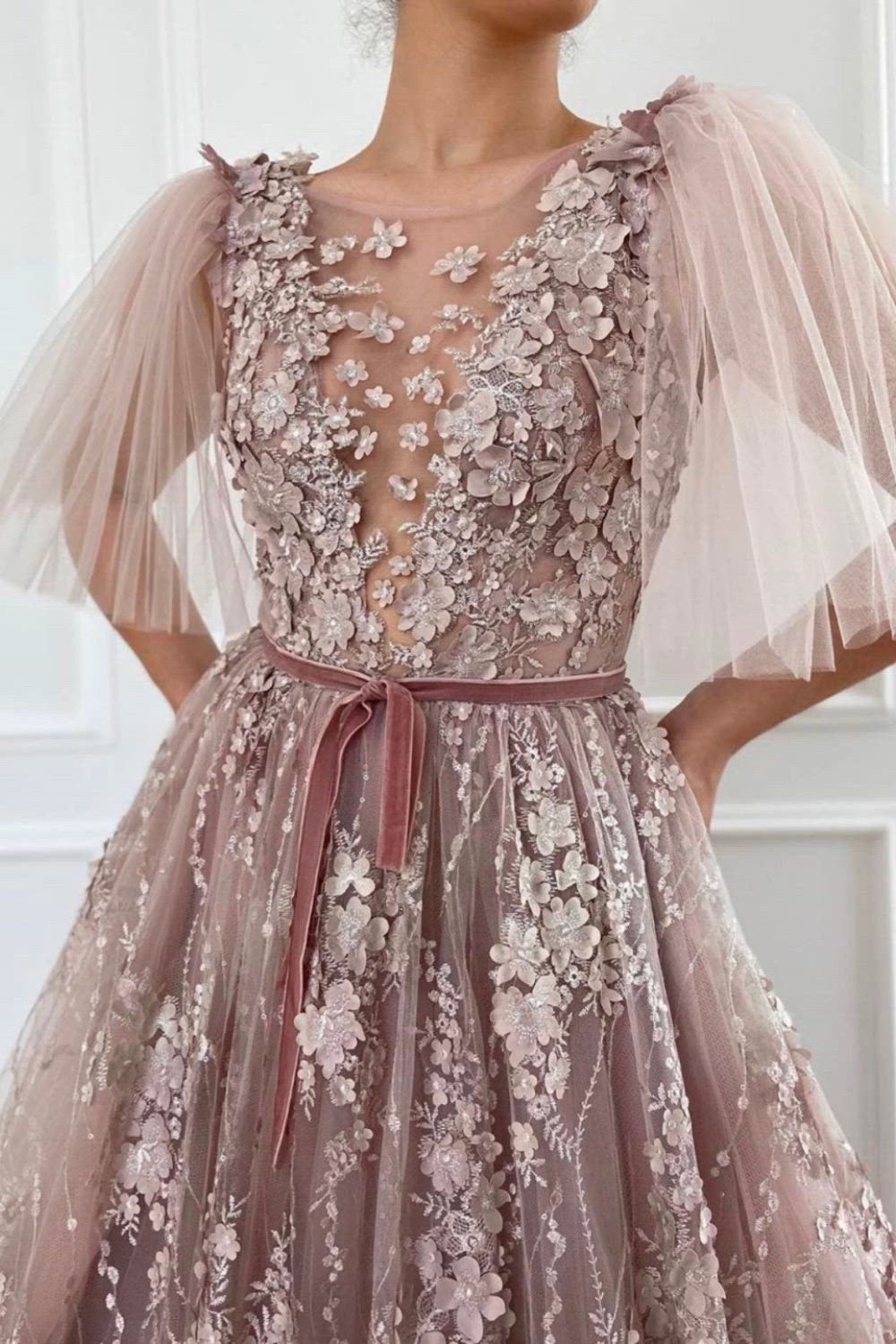 Hundreds of flower petals in the softest shade of Tuscan pink cover the Flower Petals Embroidered Gown. The dress is made of embroidered lace and tulle fabrics with sheer flowing sleeves. A velvet sash belt adds waist definition. This dress is perfect for a summer garden party or any other formal occasion.