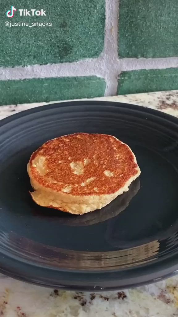 This may contain: a stack of pancakes sitting on top of a black plate next to a green wall