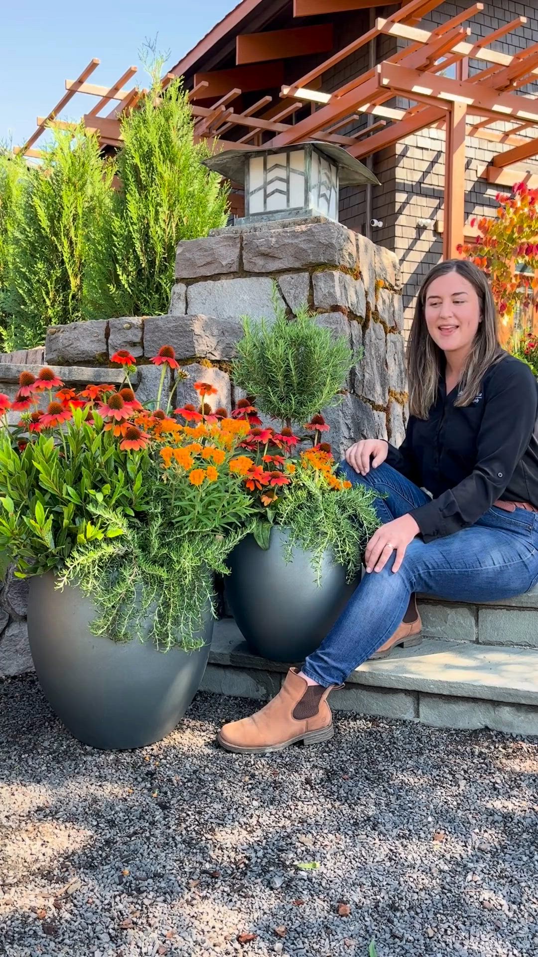 This may contain: a woman sitting on the steps next to some flowers and plants in large planters