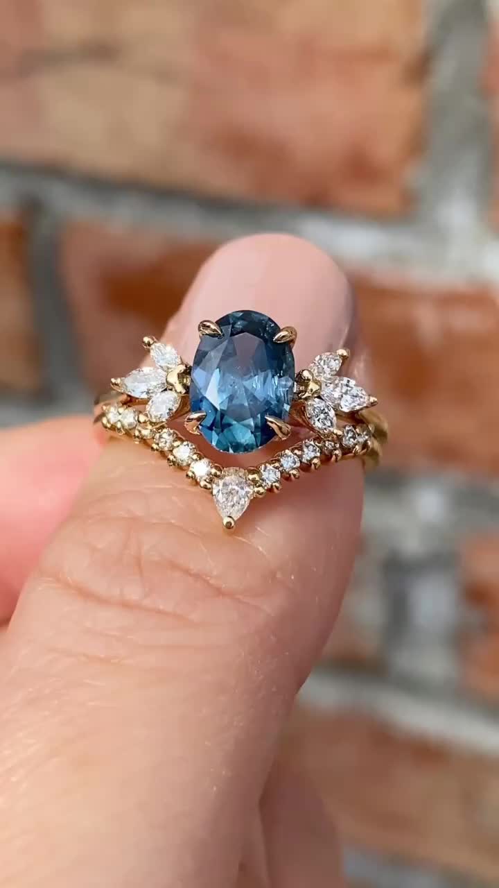 This may contain: a woman's hand holding an engagement ring with a blue stone surrounded by diamonds