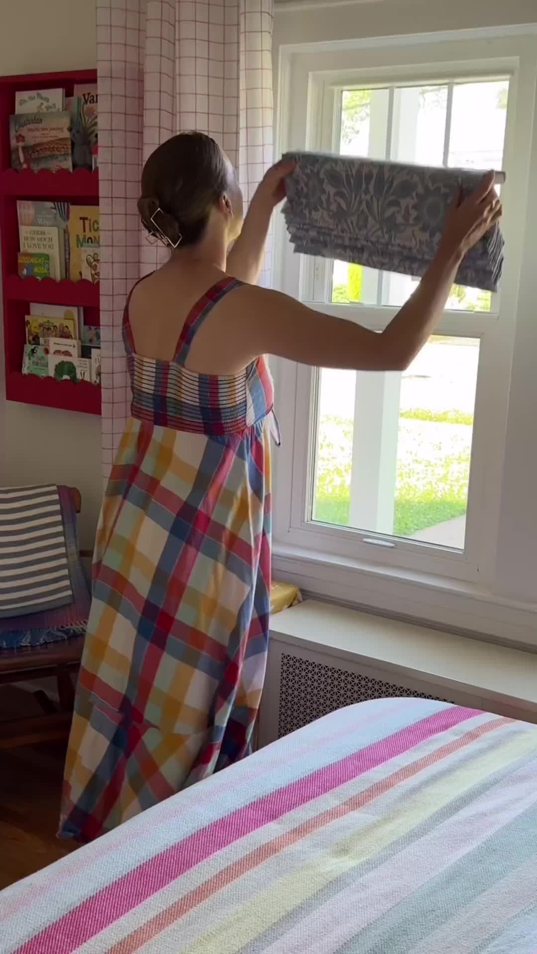 This may contain: a woman standing in front of a window with roman shades on it's windowsill